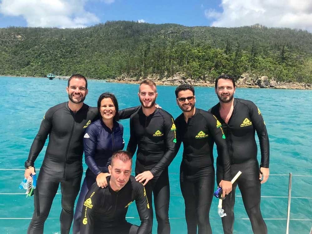 fotografía de un grupo de amigos con el neopreno y en un barco y detrás el agua cristalina